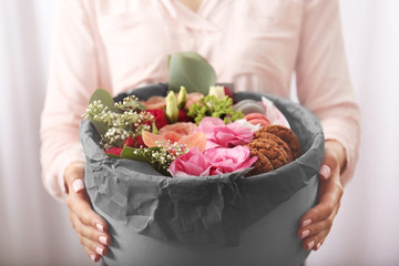 Female hands holding gift box with flowers and cookies closeup