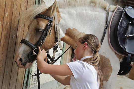 jeune fille 11 ans harnachant un poney dans une &eacute;curie 