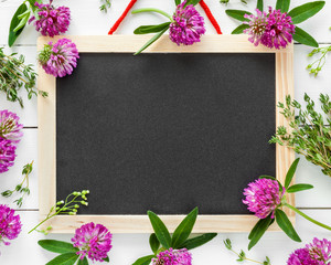Empty blackboard, floral border from flowers and herbs. Top view