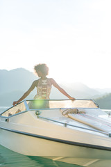 Summer vacation - young afro woman driving a motor boat on sunse