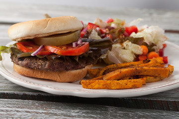 Freshly grilled hamburger with cheddar cheese, organic tomatoes and lettuce, red onion, dill pickle and toasted bun with homemade oven baked sweet potato fries with an organic salad on the side whole