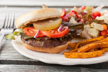 Wood table - Freshly grilled hamburger with cheddar cheese, organic tomatoes and lettuce, red onion, dill pickle and toasted bun with homemade oven baked sweet potato fries with an organic salad