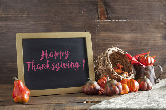 Happy Thanksgiving Written In Red Chalk On Black Chalkboard Background On Aged Wood Table With Thanksgiving Decorations In Selective Focus.
