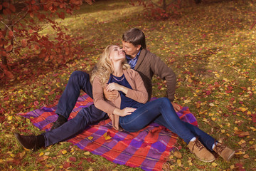 Happy young couple sit on a plaid in park in the fall