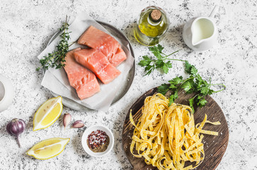 Fototapeta na wymiar Ingredients for cooking lunch - raw salmon, dry pasta tagliatelle, cream, olive oil, spices and herbs. On a light background, top view