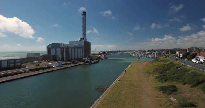 Aerial pull out view of a power station between a river and the sea
