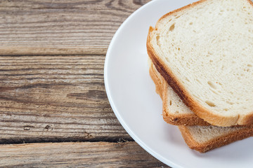 A stack of white bread slices on a plate on a wooden table.