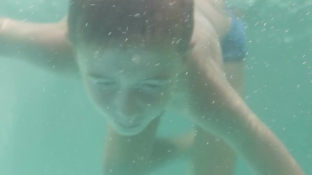 Boy dives under water in the pool with clear blue water