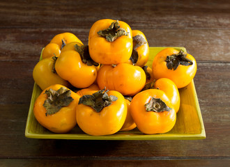 Persimmons in green tray, on old wooden table