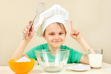 Young smiling chef at the table with ingredients is going to cook a cake