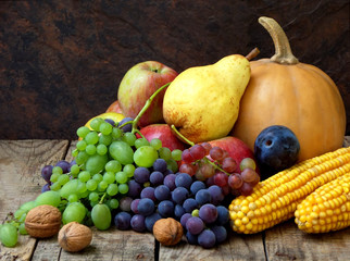 still life of autumn fruits and vegetables like grapes, apples, pears, plums, pumpkin, corn nuts on a wooden background. selective focus