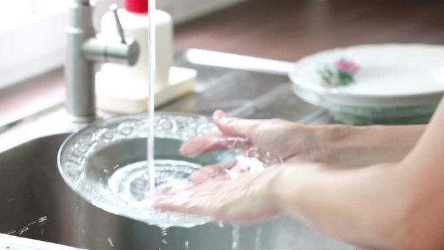 Asian Woman Hand Washing Dishes In A Sink