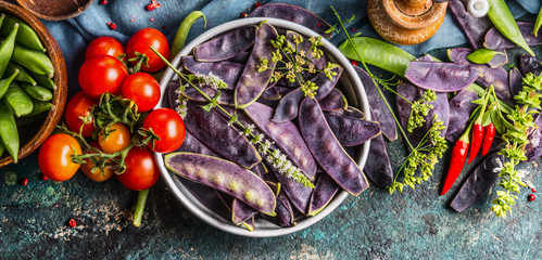 Purple pea pods in metal bowl with tomatoes and cooking ingredients, top view.  Healthy vegetarian...