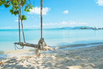 Swing under a tree by the beach on a blue sky.