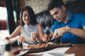 Attractive and happy young couple having good time in cafe restaurant. They are smiling and eating a pizza.