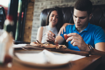 Attractive and happy young couple having good time in cafe restaurant. They are smiling and eating a pizza.