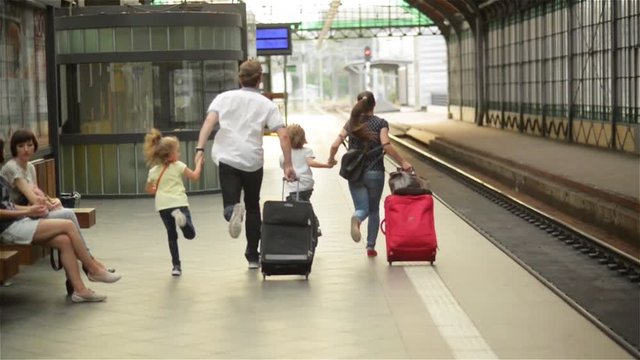 Young family of two spouses, son and daughter, running to catch the train before it leaves the railway station without them, parents and children traveling and be late