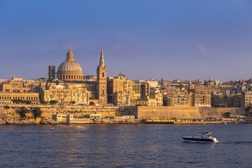 Fototapeta na wymiar Valletta, Malta - Motorboat and the famous St.Paul's Cathedral with the ancient city of Valletta at sunset