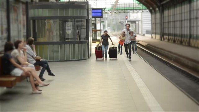 Young family of two spouses, son and daughter, running to catch the train before it leaves the railway station without them, parents and children traveling and be late