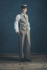 Retro 1920s dandy in suit standing with cane in front of gray wa