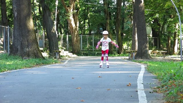 Rollerblading In The Park. Girl Rides On Roller Skates. Sports Activity. A Child On Rollers On a Track. Sport Track On The Background Of Trees