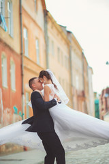 Groom gentle tilted bride, holding her in his arms and passionately kisses, wedding photo on a sunny day on a background of sand-colored walls. Newly married couple dancing in park, street tango.