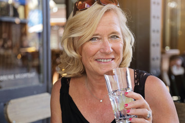 jolie femme blonde senior buvant un verre sur une terrasse en été