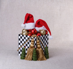 Box with Christmas balls and cap of Santa Claus decorated with a gilded cord with gold tassels and candles in the shape of Christmas trees