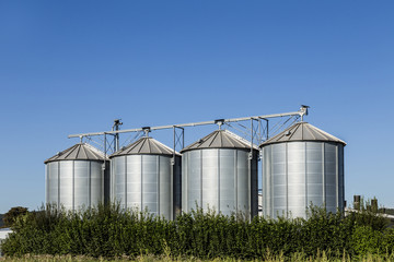 four silver silos in field under   blue sky
