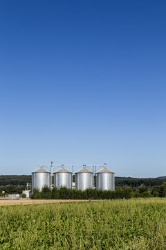 four silver silos in field under   blue sky