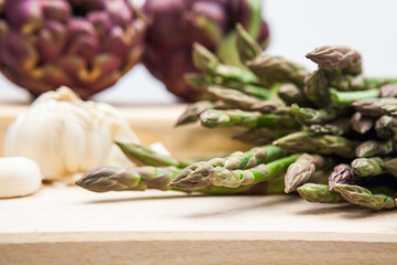 Artichokes, asparagus stems and garlic on a wooden kitchen board