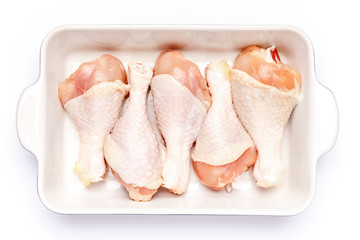 Raw chicken legs in baking dish on a white background
