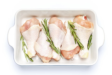 Raw chicken legs in baking dish on a white background