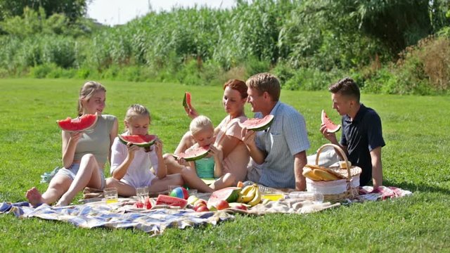 
happy man and woman with four kids having watermelon on picnic together
