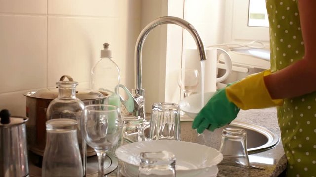 Close up photo of housewife in rubber gloves washing dishes in the kitchen