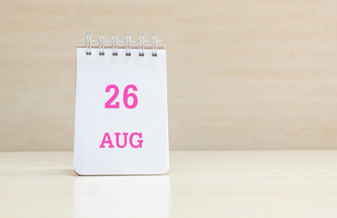 Closeup surface note book with pink 26 aug word  in page on blurred brown wood desk and wood wall textured background with copy space under window light