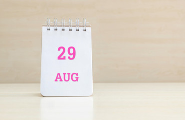 Closeup surface note book with pink 29 aug word  in page on blurred brown wood desk and wood wall textured background with copy space under window light