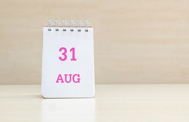 Closeup surface note book with pink 31 aug word  in page on blurred brown wood desk and wood wall textured background with copy space under window light