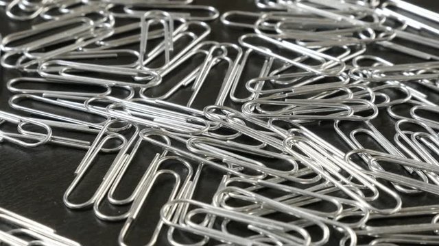 Lot of metal or steel wire clips for documents in office on wooden table close-up slow tilt 4K 2160p 30fps UltraHD footage - Wire steel paperclips with looped shape 4K 3840X2160 UHD tilting video 