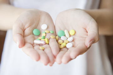 Woman is holding a lot of different pills in both her  hands