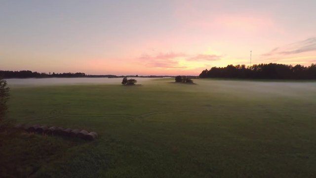 Evening fog over green field. Aerial footage. Beautiful sunset with colorful sky.