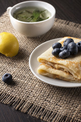 delicious fragrant breakfast at the kitchen table: a hot cup of tea, fried pancakes, blueberries, star anise, lemon