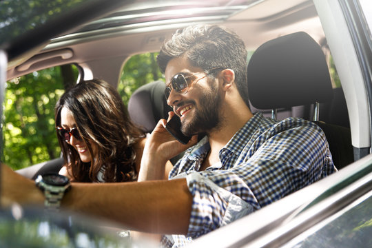 Portrait of young couple driving a car. He talking on the phone while driving
