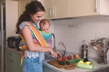 Foto auf Acrylglas Kochen Young mom cooking in the kitchen with the baby. Vegetarian healthy food. Healthy food breastfeeding mothers.