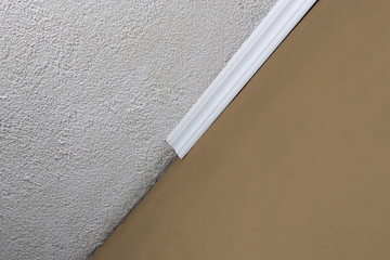Installing crown molding on ceiling in room with painted wall. Fragment of molding, horizontal view.