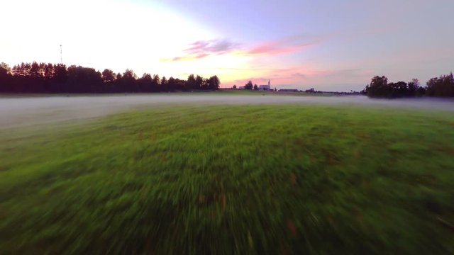 Evening fog over green field. Aerial footage. Beautiful sunset with colorful sky.