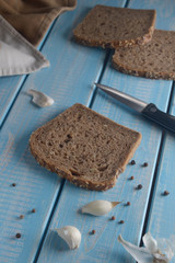Slices of rye bread with sesame seeds, and garlic on blue wooden table.