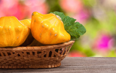 yellow pattypan squash with leaf in a wicker basket on wooden table blurred background