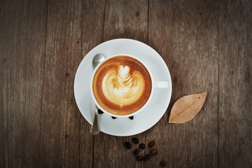 Cup of art latte or cappuccino coffee on wood table background, top view