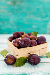 Ripe plums in a basket on a wooden table.
